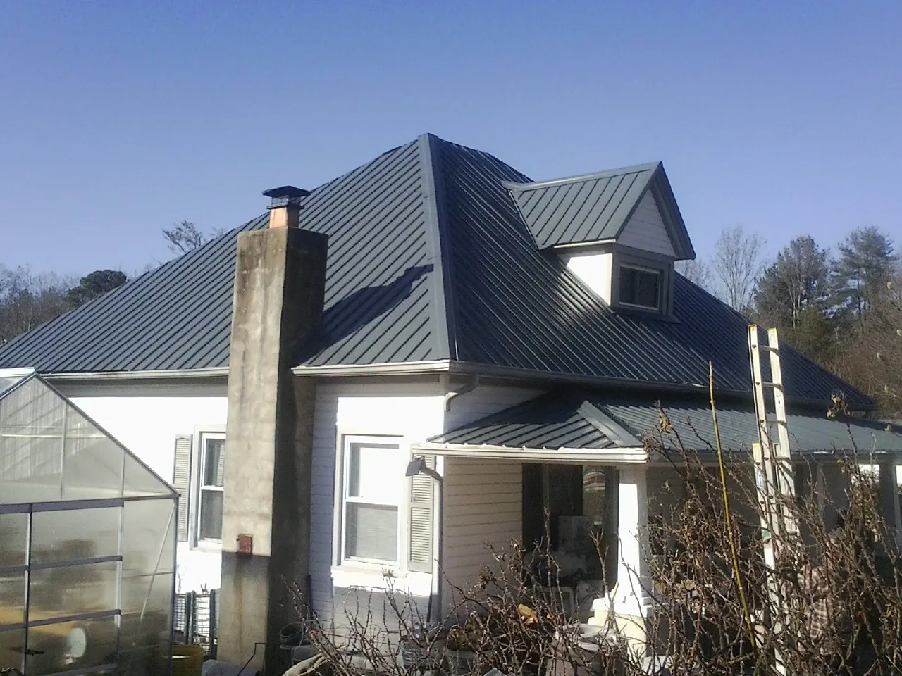 Dark blue standing seam metal roof on a white farmhouse with dormer — Slate & Tile Roof Repair by Roofing Brothers in Burlingame