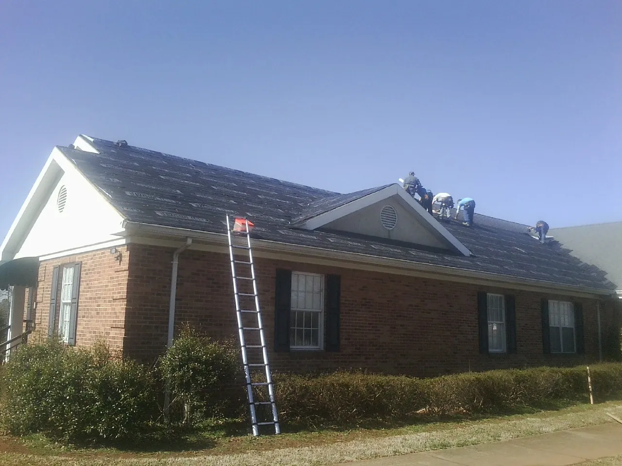 Crew tearing shingles off a brick ranch roof with a ladder set — Metal Roof Repair work by our crew in Burlingame