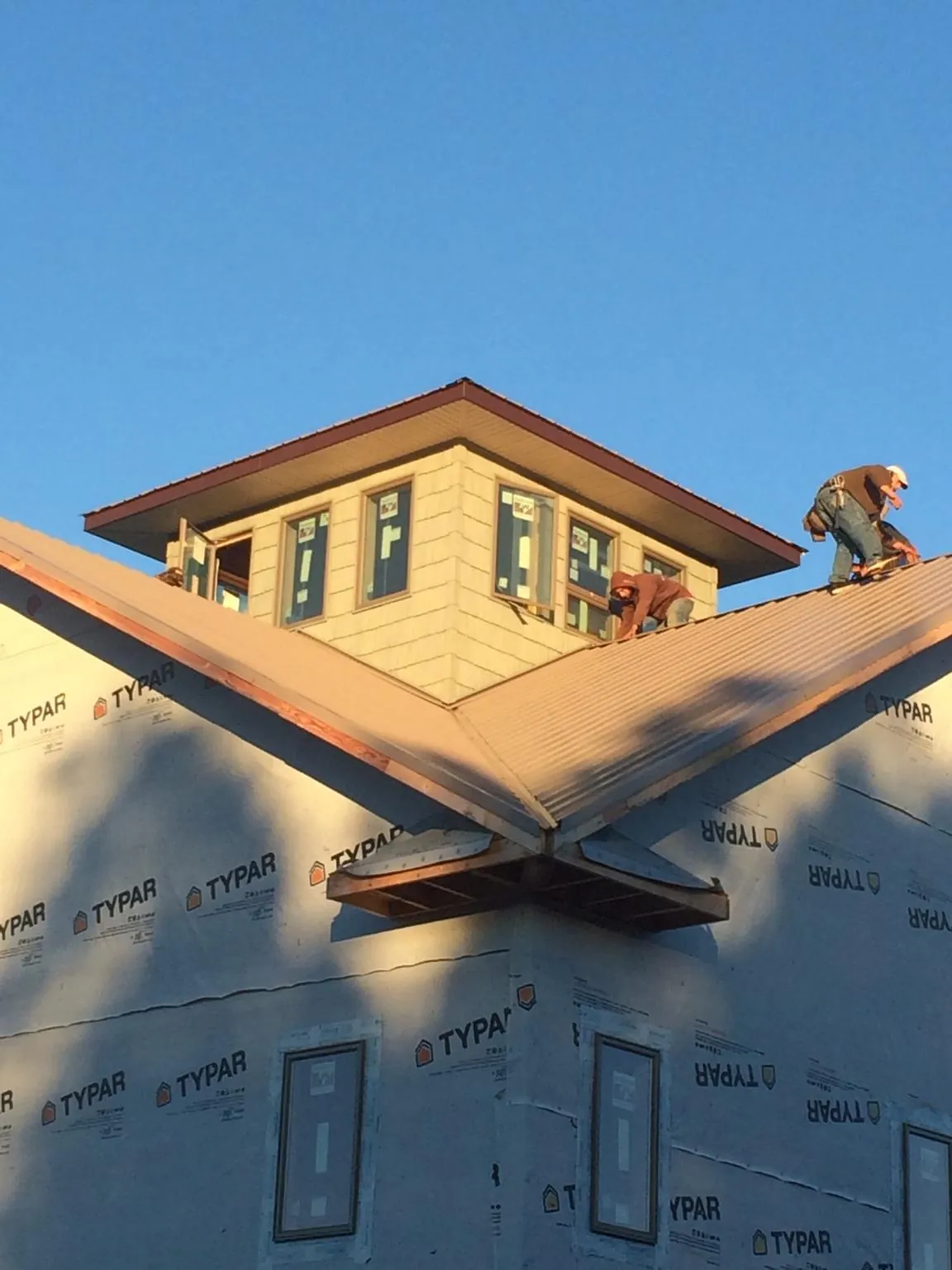 Roofers working around a rooftop cupola on a new metal roof at sunset in Burlingame